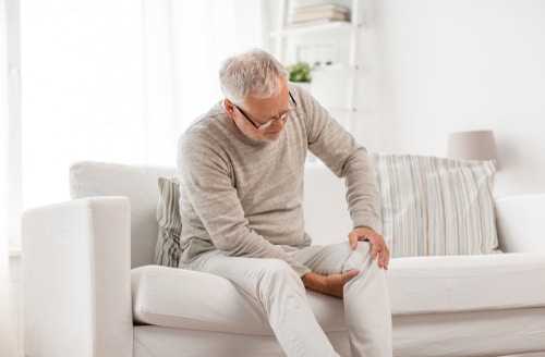 Older man on couch holding knee in pain