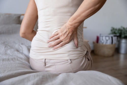 Older woman sitting on bed touching back in pain