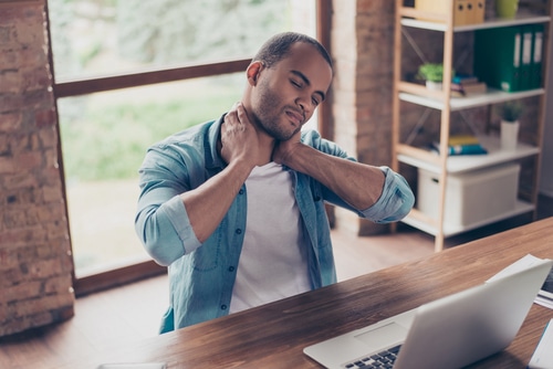 Young man at desk suffering from neck pain