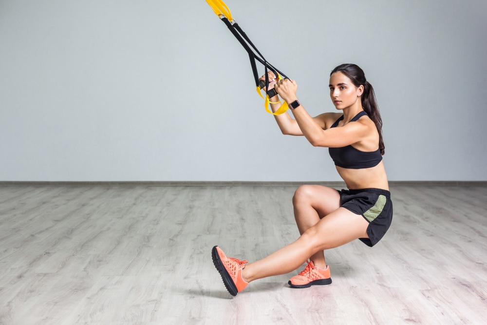 Young woman using TRX in gym